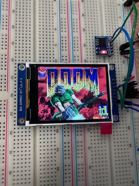 A 2.4-inch colour TFT panel on a breadboard displaying the DOOM title screen, wired to a microcontroller with jumper leads.