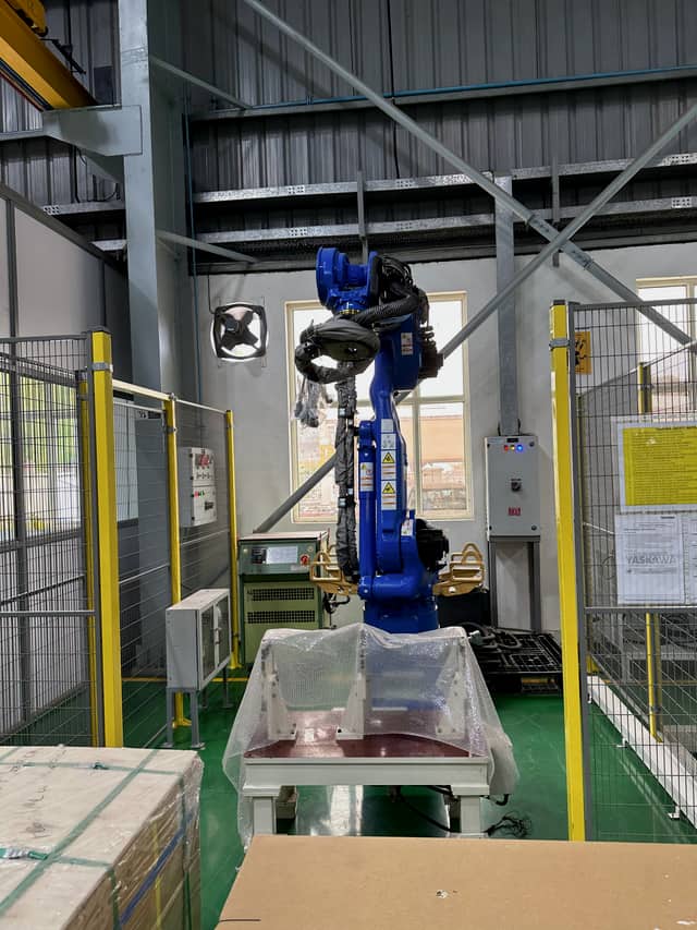 An industrial robot inside a yellow safety fence, with its controller and an interlocked gate.
