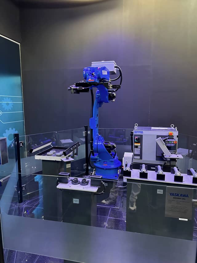 A robot arm carrying a multi-tool head above a bench holding a tray of small circular parts.