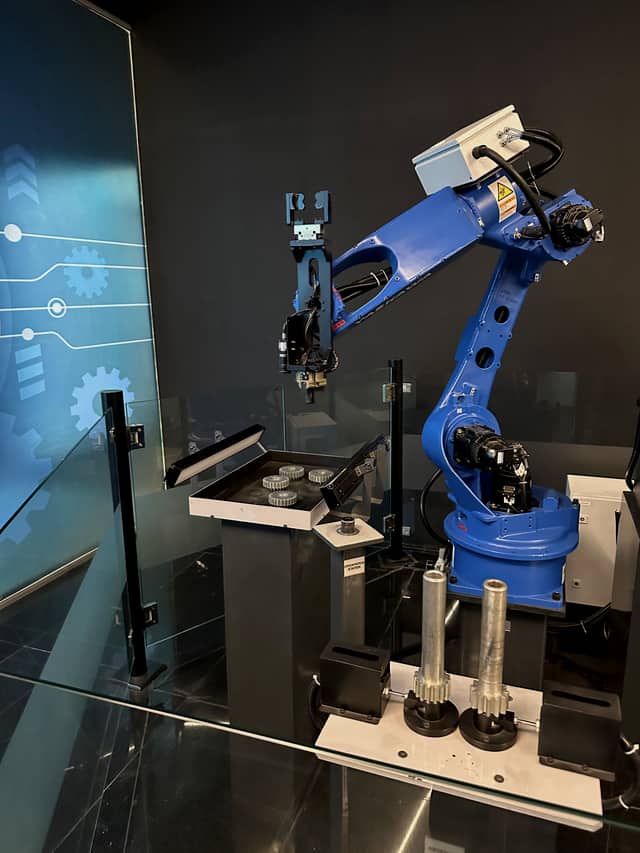 A robot arm reaching over a tray of ridged bottle caps, with bottles staged in the foreground.